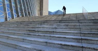 Bisiklete binen bir kadın, parkta merdivenlerde numara yapıyor.