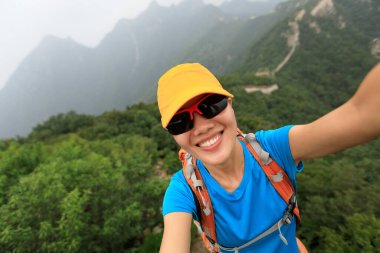 Young woman hiker taking photo with smart phone on top of great wall
