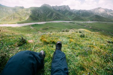 Yürüyüşçü yüksek rakımlı dağın tepesinde otur ve manzaranın tadını çıkar.