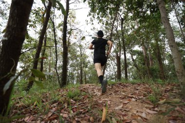 Kadın koşucu orman yolunda koşuyor.