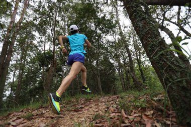 Kadın koşucu orman yolunda koşuyor.