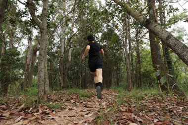 Kadın koşucu orman yolunda koşuyor.
