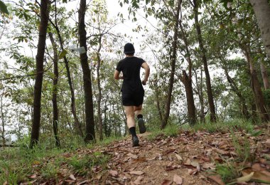 Kadın koşucu orman yolunda koşuyor.