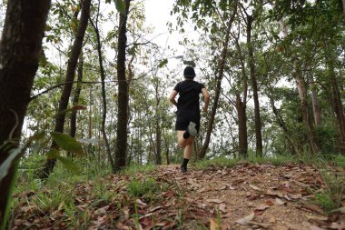 Kadın koşucu orman yolunda koşuyor.