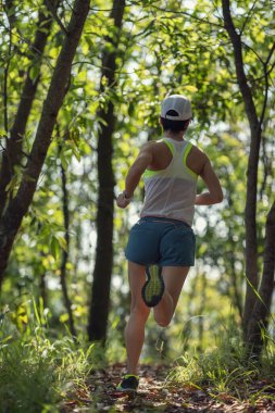 Kadın koşucu orman yolunda koşuyor.