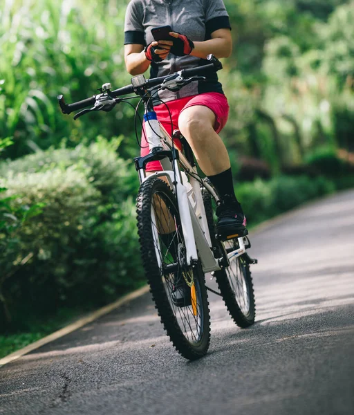 Woman using smart phone cycling on tropical park trail in summer