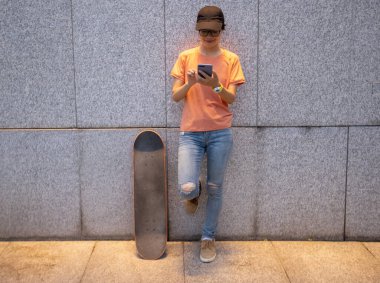 Female skateboarder using smartphone leaning on wall in city