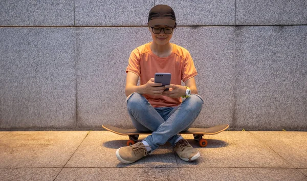 Female skateboarder using smartphone leaning on wall in city