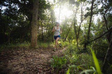 Kadın koşucu orman yolunda koşuyor.