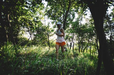 Kadın koşucu orman yolunda koşuyor.