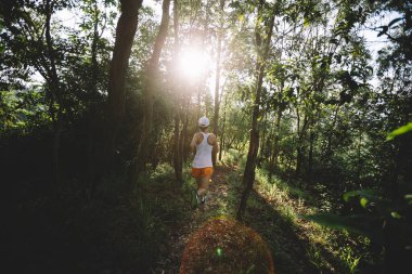 Kadın koşucu orman yolunda koşuyor.