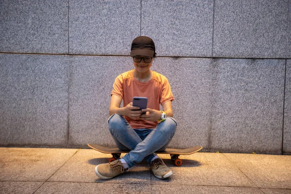 Female skateboarder using smartphone leaning on wall in city