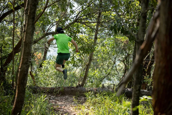 Woman trail runner running and jumping over a fallen tree trunk in tropical forest mountain 