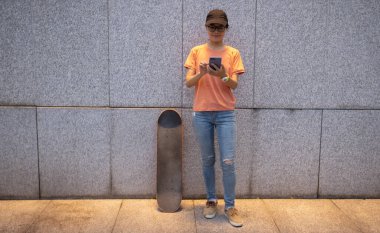 Female skateboarder using smartphone leaning on wall in city
