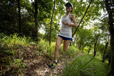 Kadın koşucu orman yolunda koşuyor.