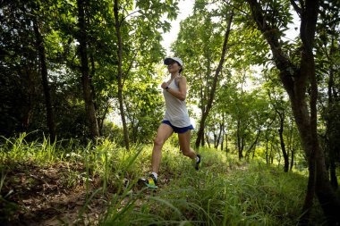Kadın koşucu orman yolunda koşuyor.