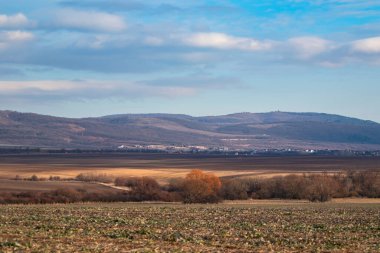 Tarlası ve dağı olan manzara ve renkli bulutlu gökyüzü