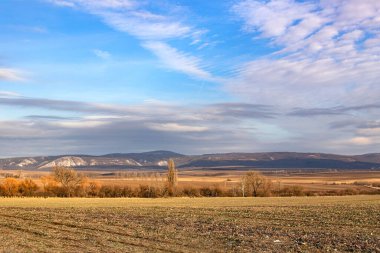 Tarlası ve dağı olan manzara ve renkli bulutlu gökyüzü