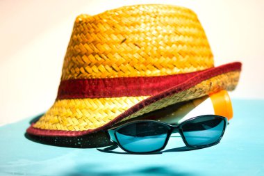 Plaj tatili için erkek sarı hasır şapka ve güneş gözlüğü açık bir arka planda izole edilmiş.