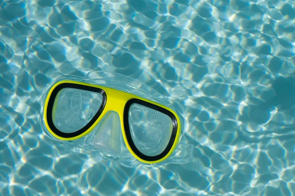 Um snorkel amarelo óculos de natação flutuando em uma piscina ondulada azul claro — Fotografia de Stock