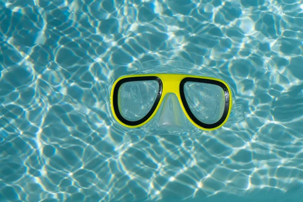 Желтые очки для плавания с маской и трубкой, плавающие в прозрачном голубом бассейне — стоковое фото