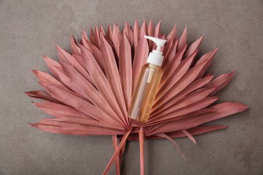 Şişe ve kurutulmuş pembe palmiye yapraklarıyla doğal güzellik ürünü.