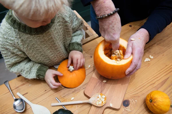 Un niño pequeño y la abuela tallan una decoración de calabaza de halloween juntos —  Fotos de Stock