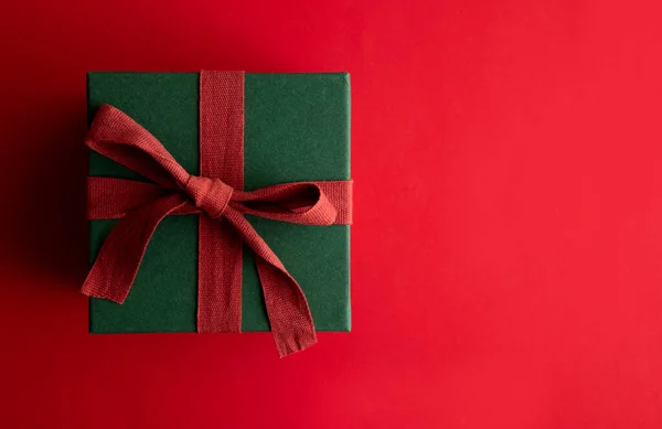 Caja de regalo navideña festiva regalo atado con una cinta rústica y lazo sobre un fondo rojo. Vista aérea — Foto de Stock