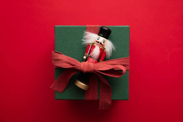 हाथ से स्टाइलिश क्रिसमस उपहार बॉक्स मौजूद है। बॉक्स लाल रिबन और एक उत्सव नटक्रैकर खिलौना से बंधे हुए — स्टॉक फ़ोटो, इमेज