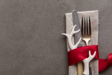 Geyik boynuzu süslemeli kırmızı bir kurdeleye sarılı sofra takımı.