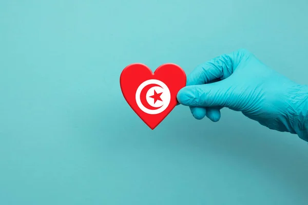 Medical workers hand wearing surgical glove holding Tunisia flag heart — Stock Photo, Image