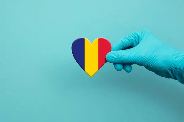 Pracownicy medyczni noszący rękawicę chirurgiczną trzymającą serce rumuńskiej flagi — Zdjęcie stockowe