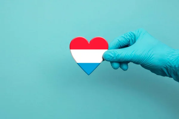 Ιατρικές εργάτριες χέρι φορώντας χειρουργικό γάντι κρατώντας τη σημαία Λουξεμβούργου καρδιά — Φωτογραφία Αρχείου