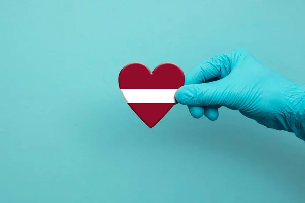 Trabajadores médicos mano usando guante quirúrgico sosteniendo bandera de Letonia corazón — Foto de Stock
