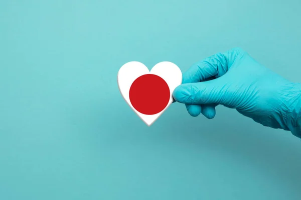 Médicos mano usando guante quirúrgico sosteniendo bandera de Japón corazón — Foto de Stock