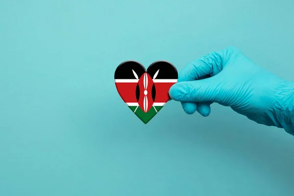 Trabajadores médicos mano usando guante quirúrgico sosteniendo bandera de Kenia corazón —  Fotos de Stock