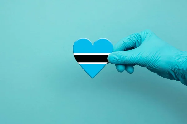 Medical workers hand wearing surgical glove holding Botswana flag heart — Foto Stock