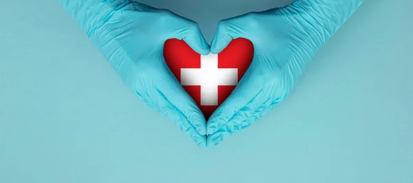 Doctors hands wearing blue surgical gloves making hear shape symbol with switzerland flag.