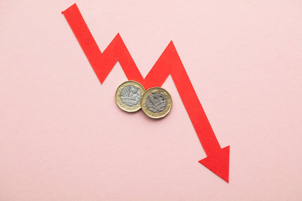 British pound sterling coins with a red downward arrow. Uk economic crisis.