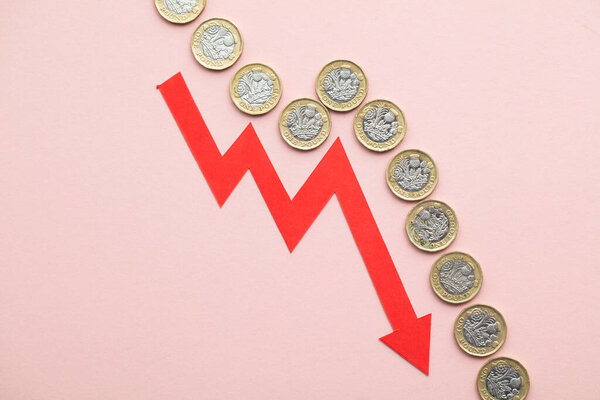 British pound sterling coins with a red downward arrow. Uk economic crisis.