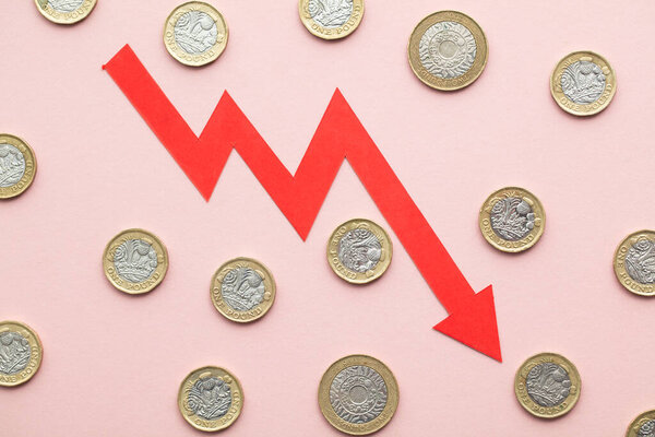 British pound sterling coins with a red downward arrow. Uk economic crisis.