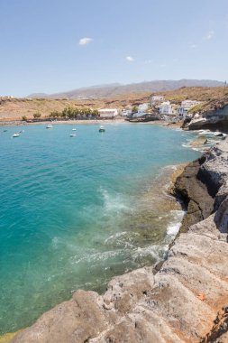 Geleneksel balıkçı koyunun manzarası, balıkçıların evleri, geleneksel balıkçı tekneleri ve kum ve arka planda dağlar olan çakıl taşı plajı..