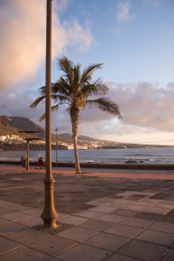 Avlu güvertesinde gün batımı ön planda bir sokak lambası ve arka planda okyanus ve kasabayla birlikte. Punta del Hidalgo, Tenerife, Kanarya Adaları. İspanya
