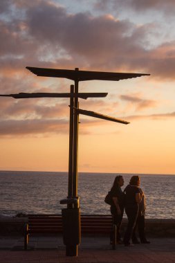 Avlu güvertesinde gün batımı ön planda bir sokak lambası ve arka planda okyanus ve kasabayla birlikte. Punta del Hidalgo, Tenerife, Kanarya Adaları. İspanya