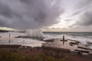 Büyük dalgaların fırtınası dalgakırana karşı kırılıyor ve Bajamar geziniyor gri fırtına bulutları ve arka planda bir deniz feneri ile.