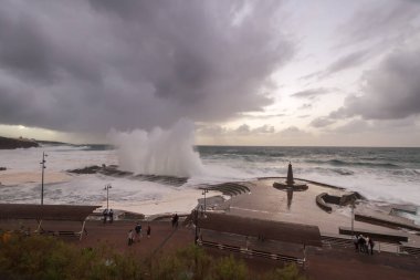 Büyük dalgaların fırtınası dalgakırana karşı kırılıyor ve Bajamar geziniyor gri fırtına bulutları ve arka planda bir deniz feneri ile.