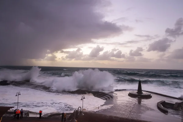 Büyük dalgaların fırtınası dalgakırana karşı kırılıyor ve Bajamar geziniyor gri fırtına bulutları ve arka planda bir deniz feneri ile.