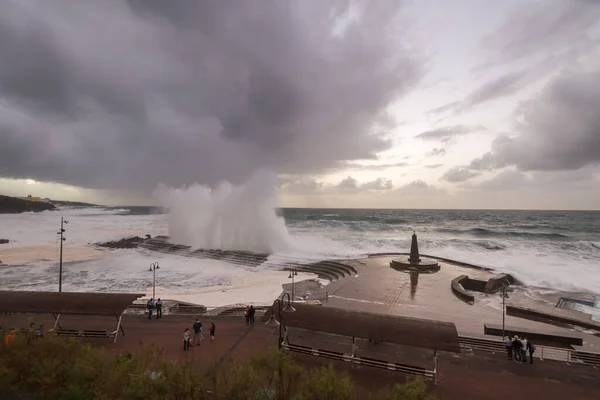 Büyük dalgaların fırtınası dalgakırana karşı kırılıyor ve Bajamar geziniyor gri fırtına bulutları ve arka planda bir deniz feneri ile.