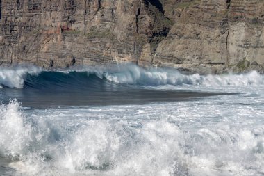 Bol köpüklü dalgalar, Atlantik Okyanusu 'nun volkanik siyah kumlu sahilinde, arka planda kayaları ve kayaları gören dalgalar. Los Gigantes, Tenerife, Kanarya Adaları 'ndan Cliff. İspanya