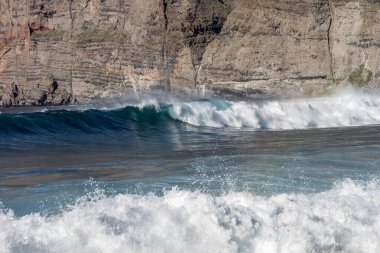 Bol köpüklü dalgalar, Atlantik Okyanusu 'nun volkanik siyah kumlu sahilinde, arka planda kayaları ve kayaları gören dalgalar. Los Gigantes, Tenerife, Kanarya Adaları 'ndan Cliff. İspanya